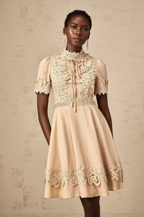 Young woman wearing a short flared dress with corded lace pattern and delicate straps standing against a plain background