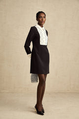 Young woman wearing a short mini dress with contrasting colors and embellishments standing in a stylish pose
