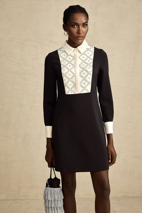 Young woman wearing a short mini dress with contrasting colors and embellishments standing in a stylish pose