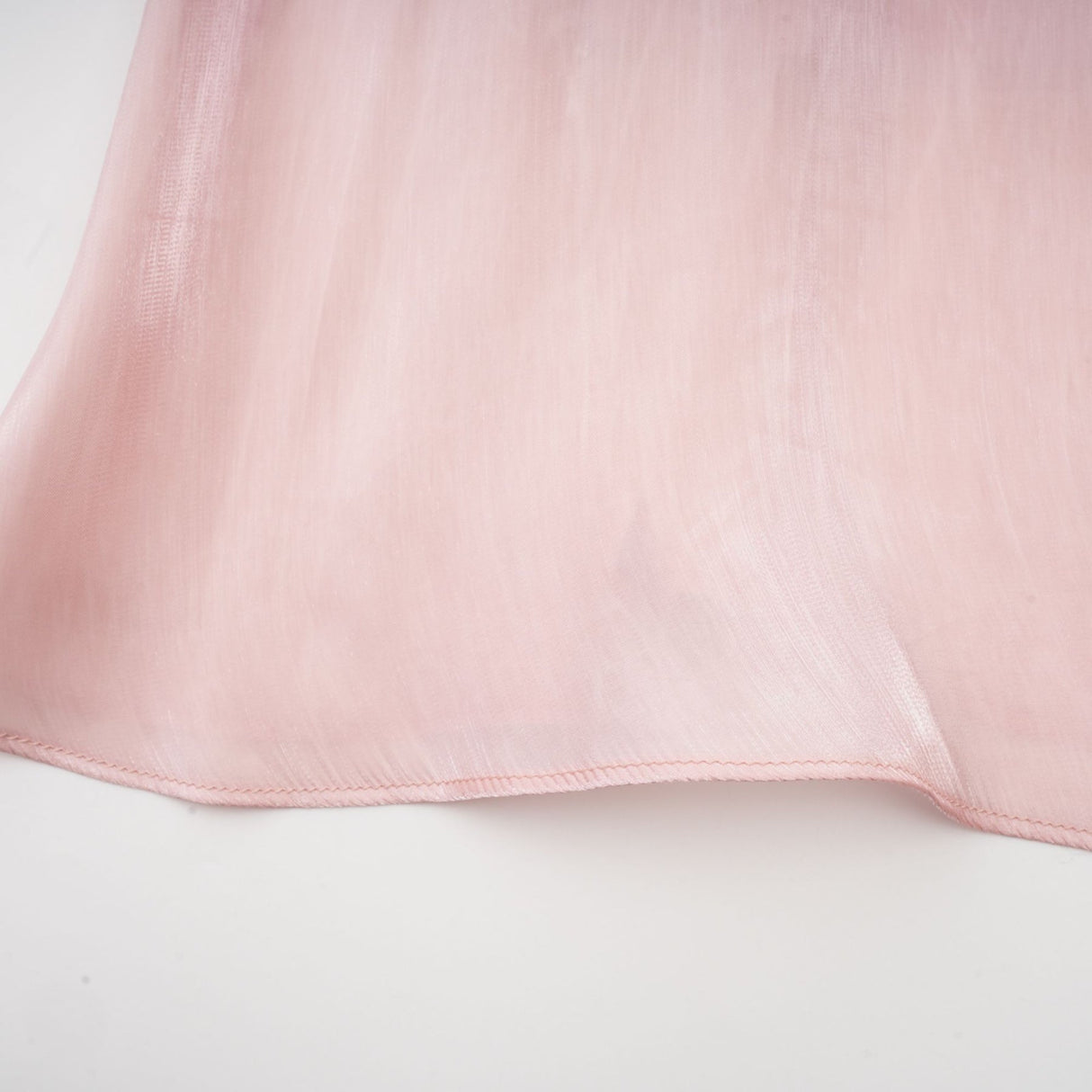 Young woman wearing a short pink dress with pleats and embellishments standing against a plain background