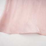 Young woman wearing a short pink dress with pleats and embellishments standing against a plain background
