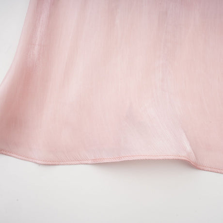 Young woman wearing a short pink dress with pleats and embellishments standing against a plain background