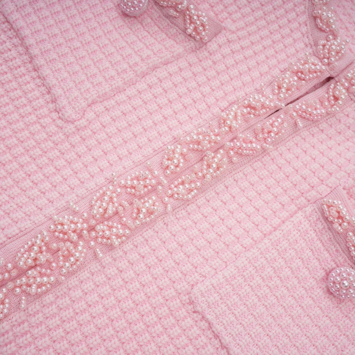 Young woman wearing a short pink knitted dress with beaded embellishments standing against a plain background