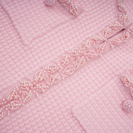 Young woman wearing a short pink knitted dress with beaded embellishments standing against a plain background