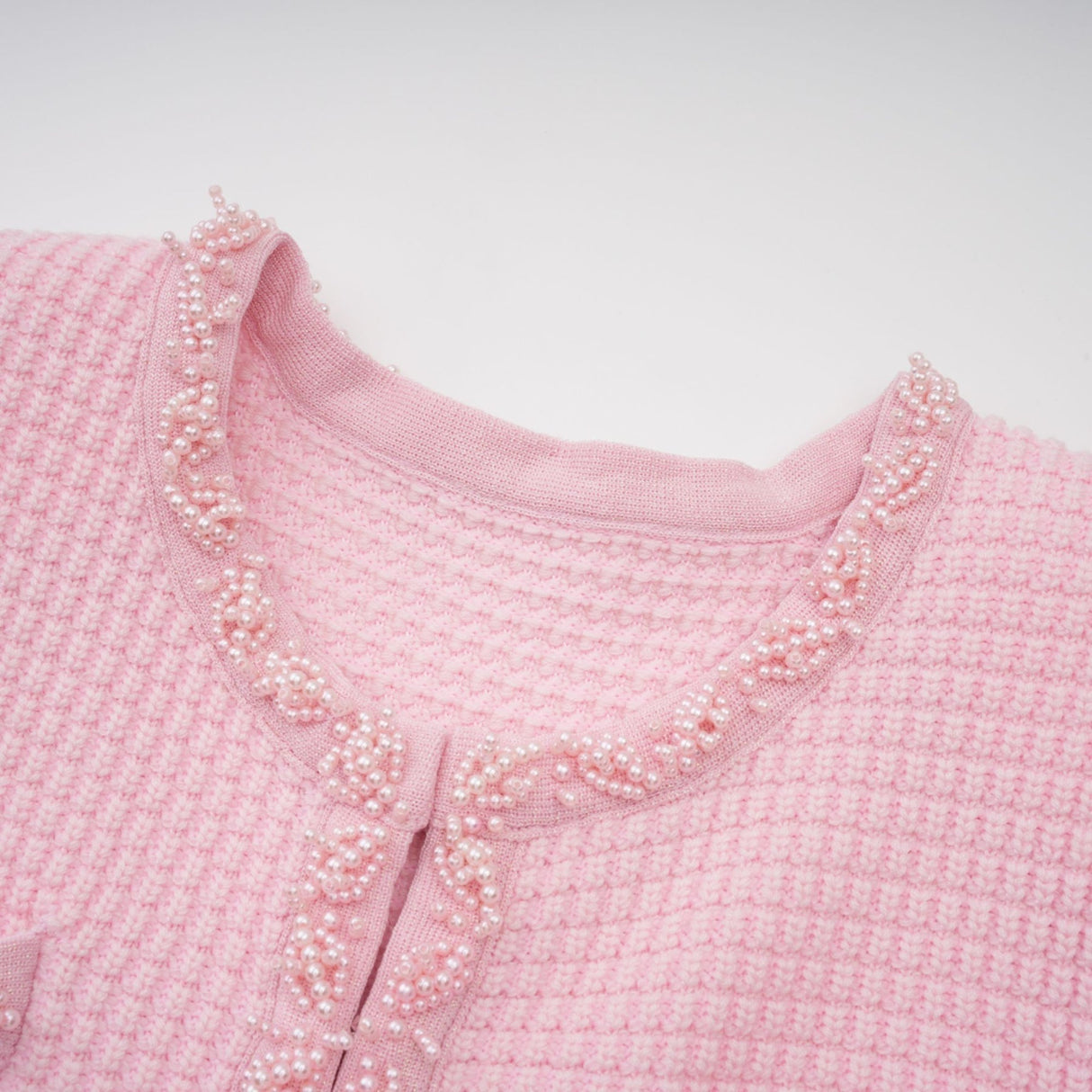 Young woman wearing a short pink knitted dress with beaded embellishments standing against a plain background
