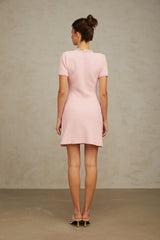 Young woman wearing a short pink knitted dress with beaded embellishments standing against a plain background