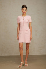 Young woman wearing a short pink knitted dress with beaded embellishments standing in a neutral background