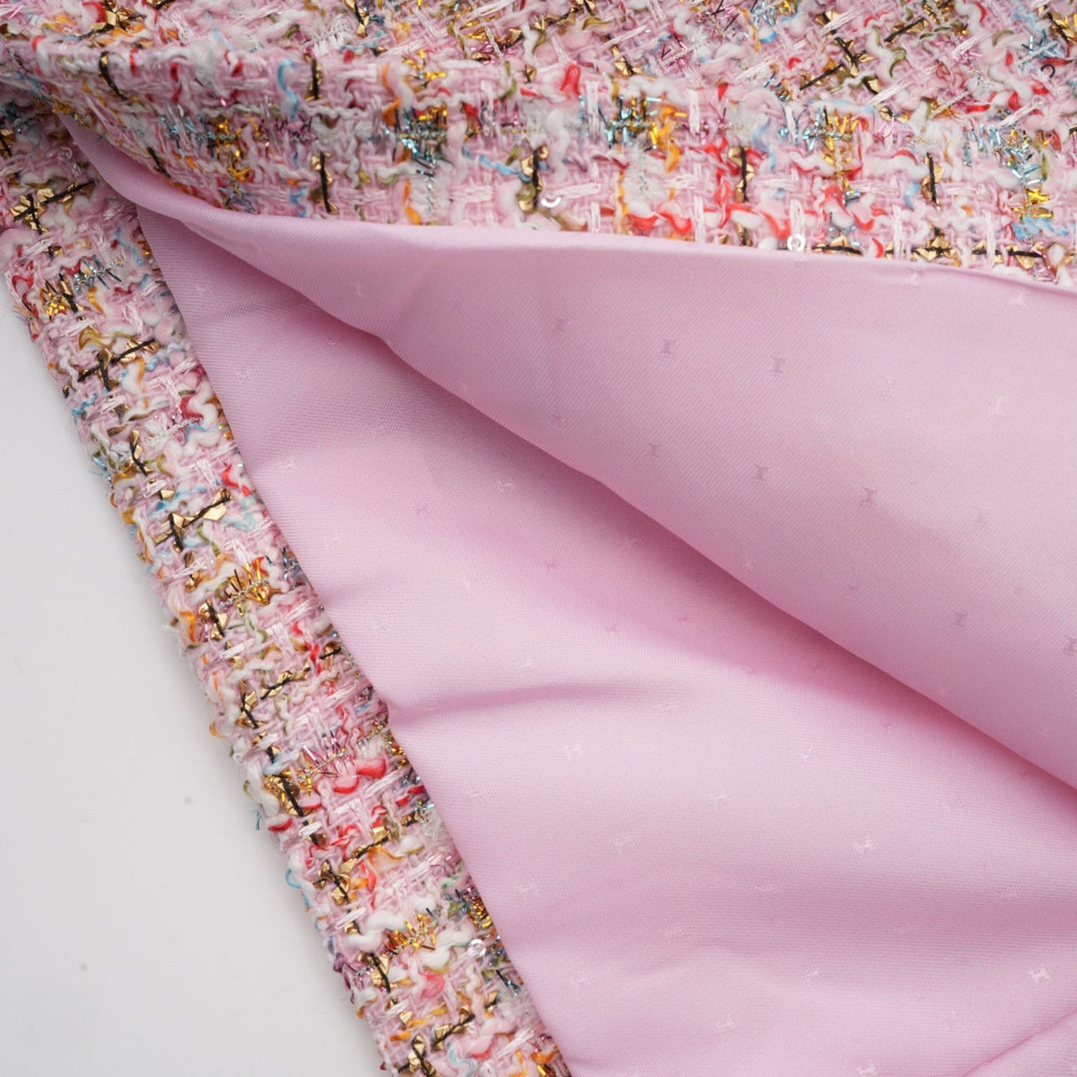 Young woman wearing a short pink tweed dress with embellishments standing against a plain background