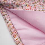 Young woman wearing a short pink tweed dress with embellishments standing against a plain background