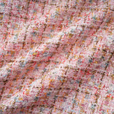 Young woman wearing a short pink tweed dress with sparkly embellishments standing against a plain background
