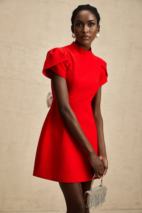 Young woman wearing a short red dress with petal sleeves and a cutout detail with a bow accent