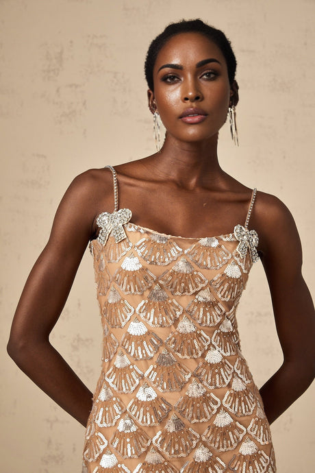 Young woman wearing a short shimmering silver dress with sequin embellishments standing against a plain background