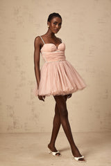 Young woman wearing a short sleeveless dress with a pleated tulle skirt in a light color against a plain background