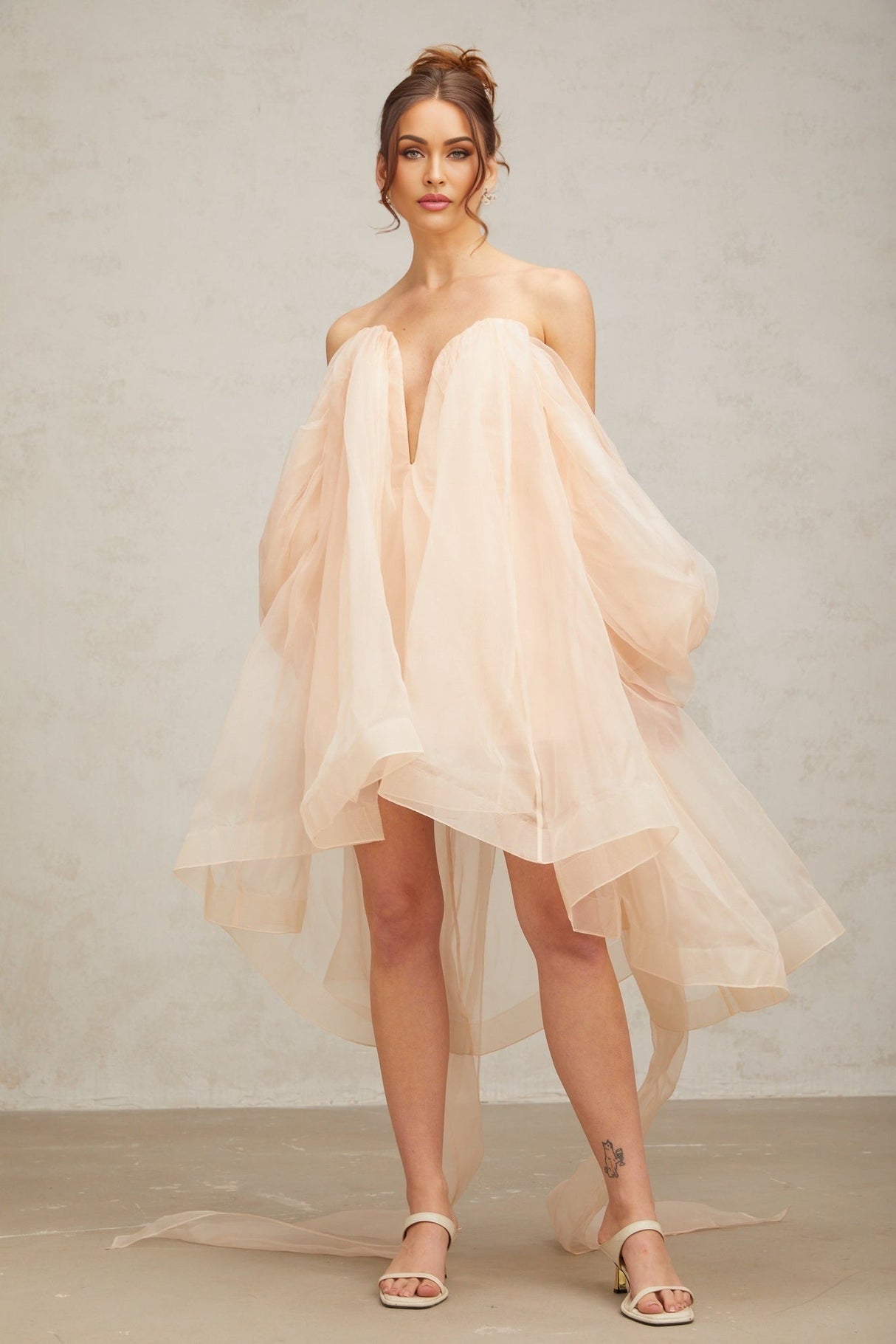 Young woman wearing a short voluminous dress with bow details and puffed sleeves in a light color