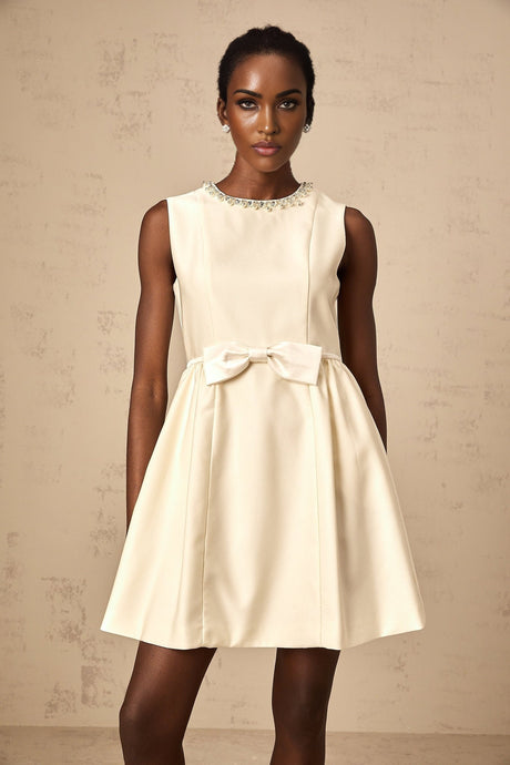 Young woman wearing a short white dress with a bowknot detail and embellishments