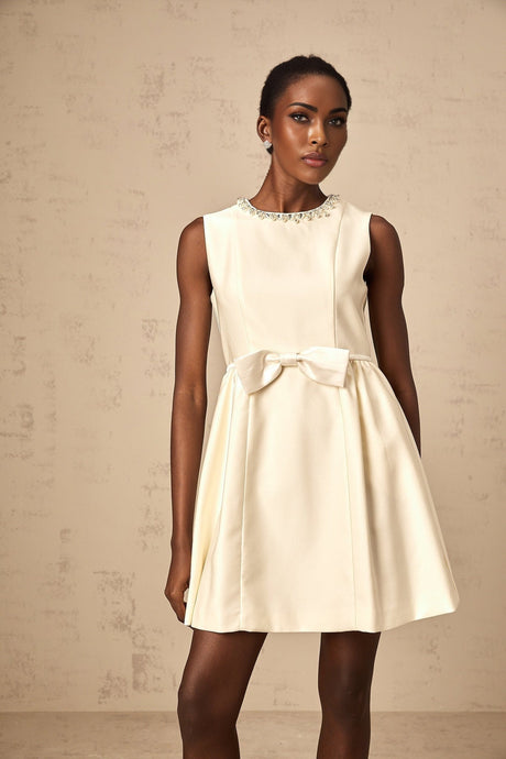 Young woman wearing a short white dress with bow detail at the waist