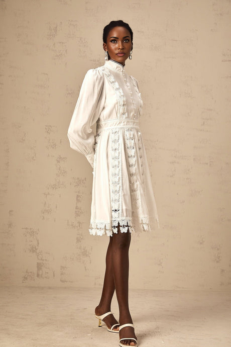 Young woman wearing a short white dress with butterfly appliques standing against a plain background