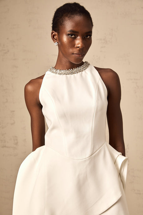 Young woman wearing a short white mini dress with crystal embellishments and layered design standing in a stylish pose