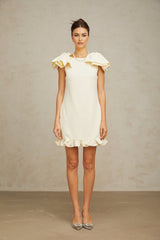 Young woman wearing a short white mini dress with ruffled details and a bow accent standing in a casual pose