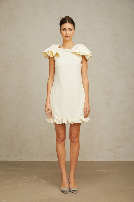 Young woman wearing a short white mini dress with ruffled details and a bow accent standing in a casual pose