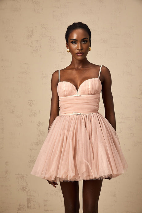 Young woman wearing a sleeveless white mini dress with pleated tulle skirt standing in a studio setting