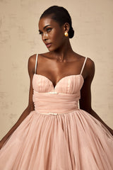 Young woman wearing a sleeveless white tulle mini dress with pleated details and a fitted bodice standing against a plain background