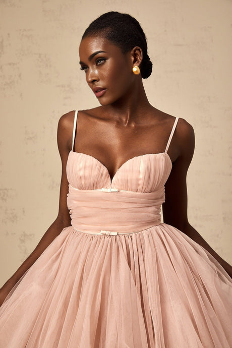 Young woman wearing a sleeveless white tulle mini dress with pleated details and a fitted bodice standing against a plain background