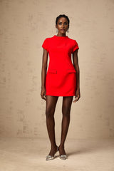 Young woman wearing a vibrant red mini dress with cap sleeves standing against a plain background