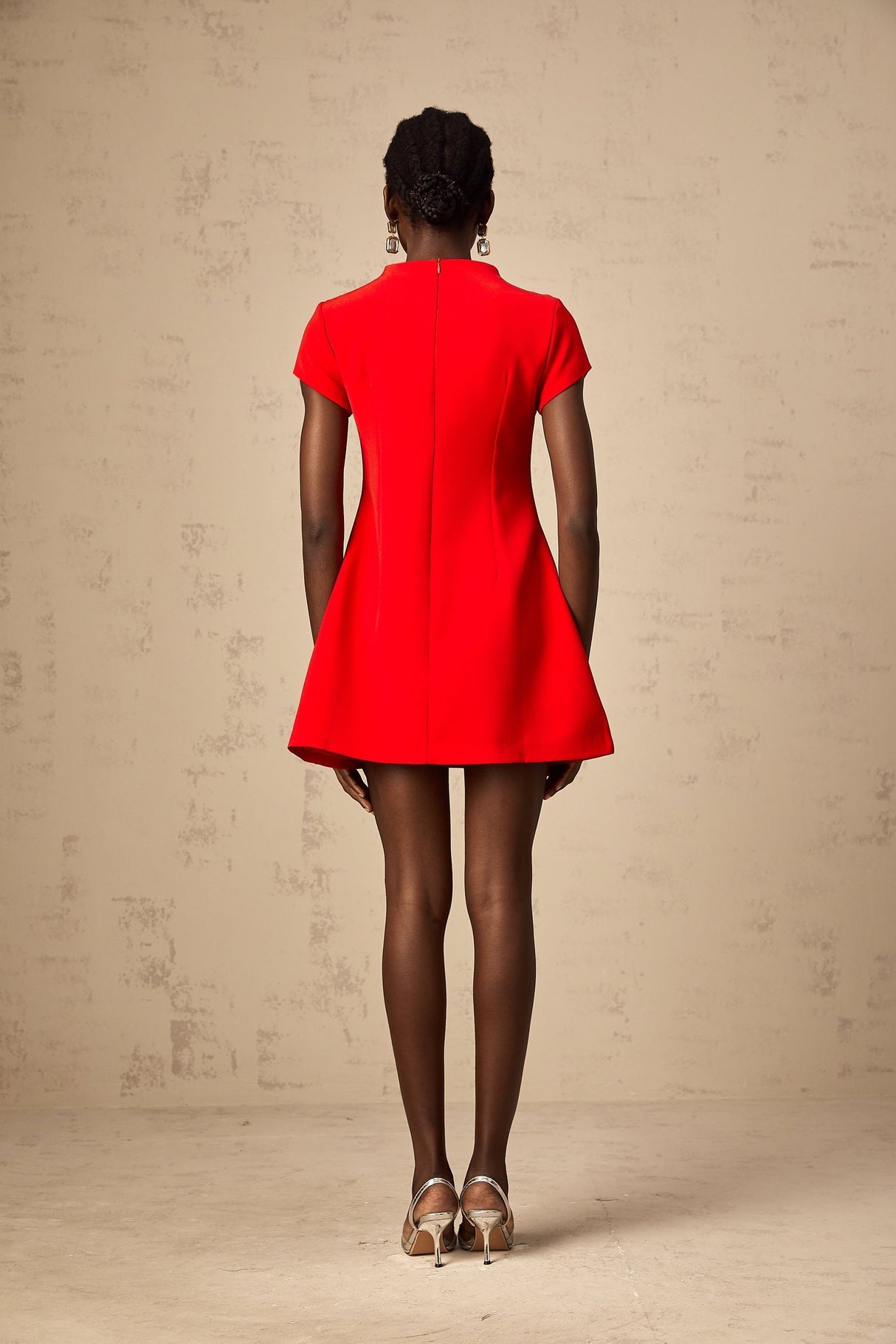 Young woman wearing a vibrant red mini dress with cap sleeves standing against a plain background