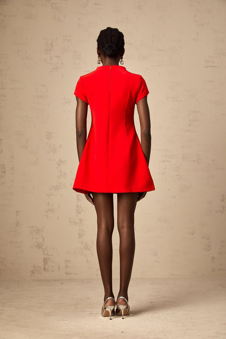 Young woman wearing a vibrant red mini dress with cap sleeves standing against a plain background