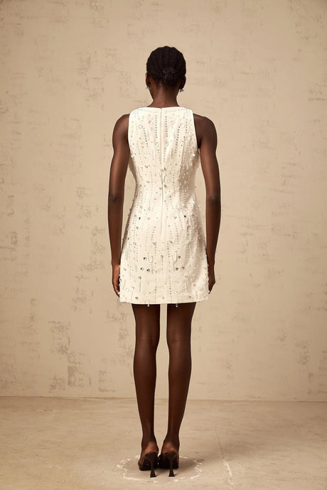Young woman wearing a white Aline mini dress with embellishments standing in a neutral background