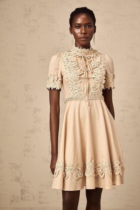 Young woman wearing a white flared mini dress with delicate corded lace pattern standing in front of a plain background