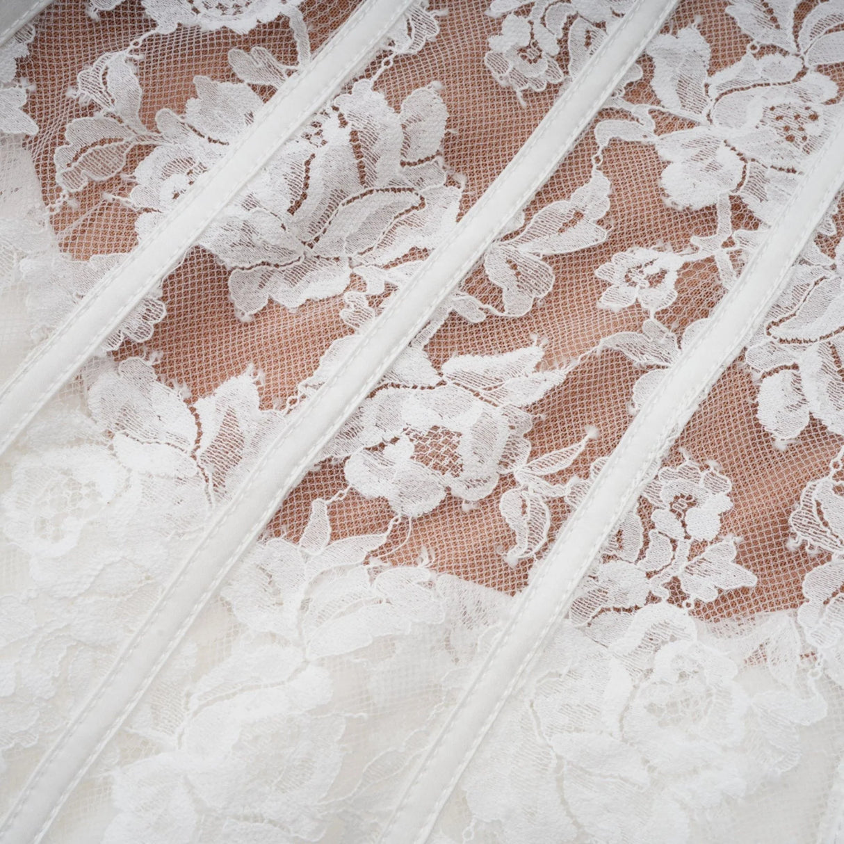 Young woman wearing a white floral lace corset mini dress with delicate straps and a fitted bodice standing against a plain background