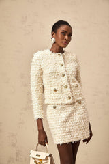 Young woman wearing a white fluffy knit cardigan and matching skirt set standing against a plain background