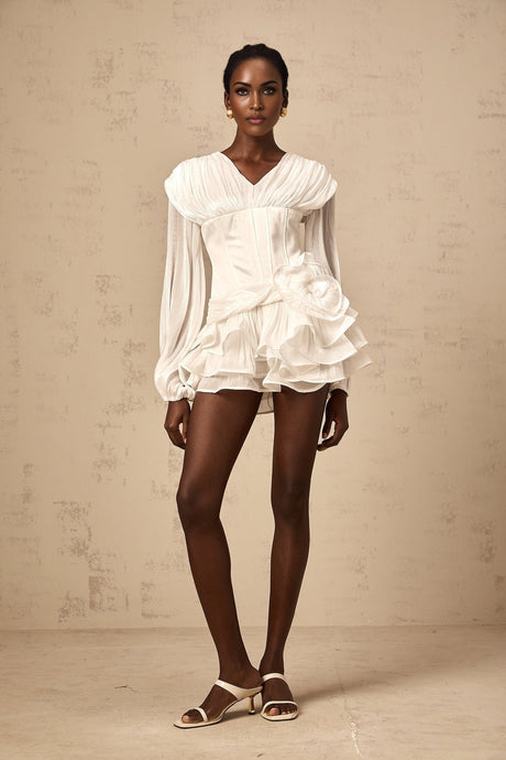 Young woman wearing a white fully pleated mini dress with cinched waist standing in front of neutral background