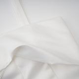 Young woman wearing a white halterneck mini dress with ruffled details standing against a plain background