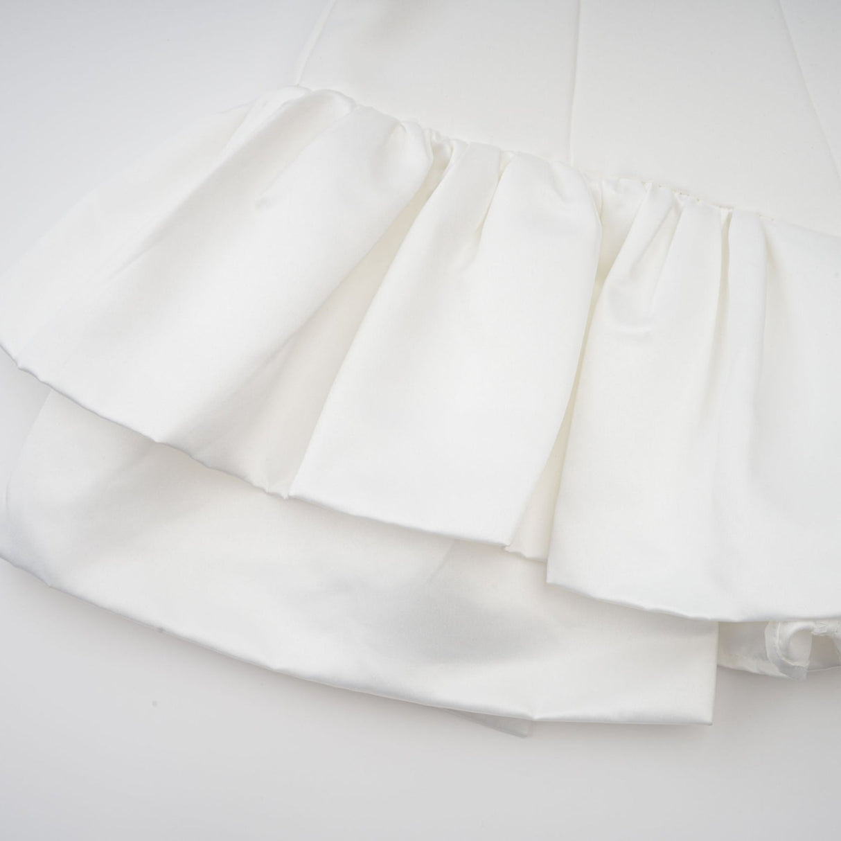 Young woman wearing a white halterneck mini dress with ruffled details standing against a plain background