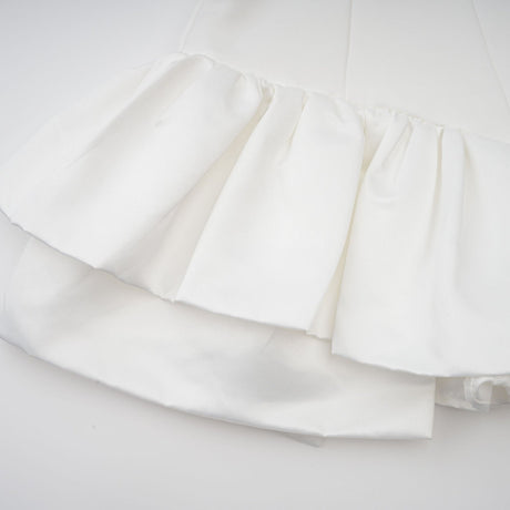 Young woman wearing a white halterneck mini dress with ruffled details standing against a plain background