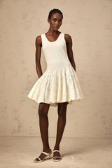Young woman wearing a white jacquard knit mini dress with textured pattern standing against neutral background