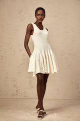 Young woman wearing a white jacquard knit mini dress with textured pattern standing against plain background