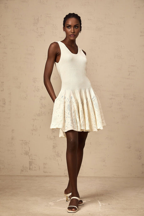 Young woman wearing a white jacquard knit mini dress with textured pattern standing against plain background