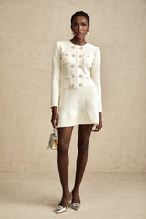 Young woman wearing a white knitted mini dress with flared skirt standing against a plain background