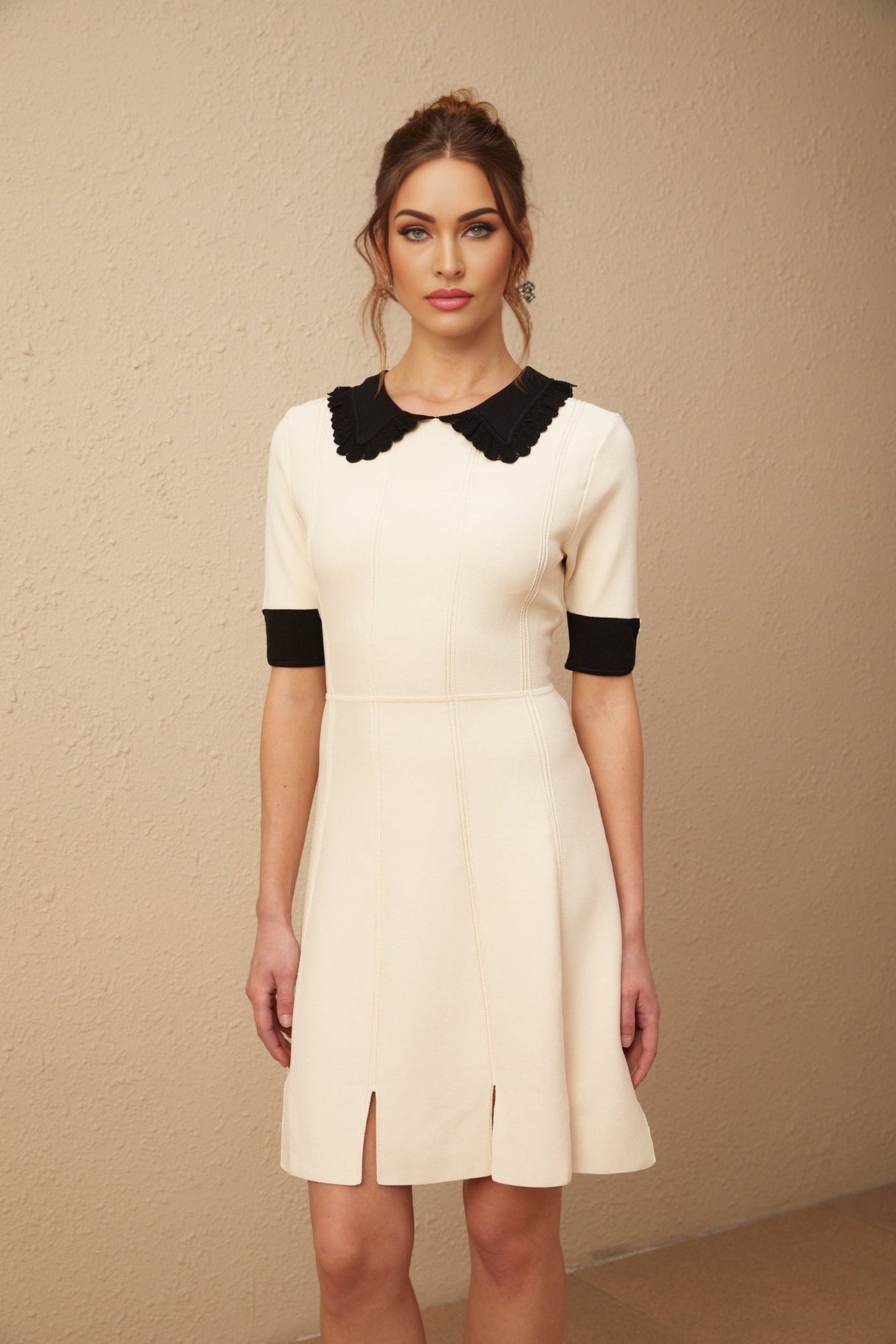 Young woman wearing a white knitted mini dress with split hem detail standing in front of plain background