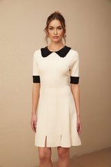 Young woman wearing a white knitted mini dress with split hem detail standing in front of plain background