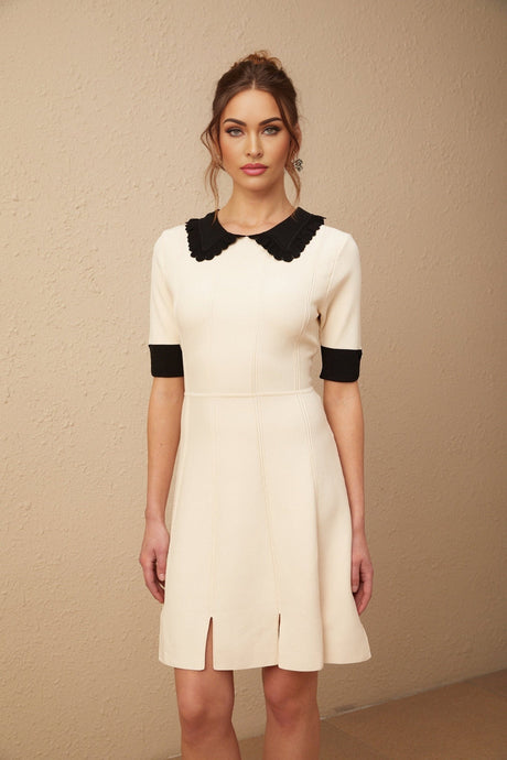 Young woman wearing a white knitted mini dress with split hem detail standing in front of plain background