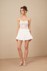 Young woman wearing a white lace matching set consisting of a top and skirt standing against a plain background