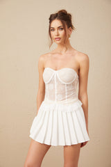 Young woman wearing a white lace matching set consisting of a top and skirt standing against a plain background