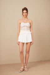 Young woman wearing a white lace matching set with a crop top and skirt standing against a plain background