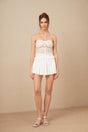 Young woman wearing a white lace matching set with a crop top and skirt standing against a plain background