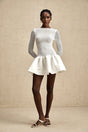 Young woman wearing a white lace mini dress with panels standing in front of a light background